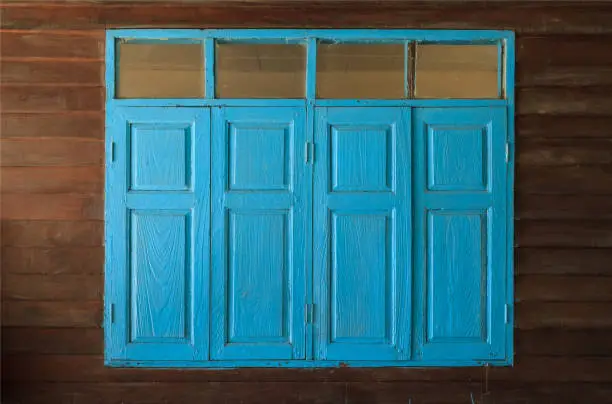 light blue painted vintage retro wooden windows and panes, home interior architectural design against plain tropical dark brown textured wood panel board wall in old Asian house