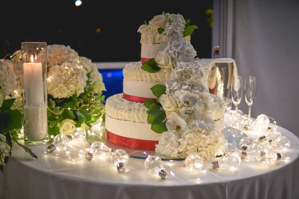 istock A three-tiers white wedding cake with rose decors on a table decorated with white candles and light bulbs. 1019033988