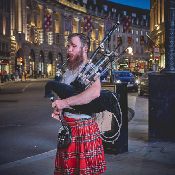 London, UK - August, 2018. Scottish bagpipe player performing in Piccadilly Circus at night.