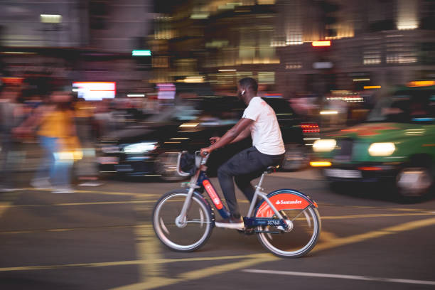 A commuter cycling on a Santander Cycles bikes, also known as Boris bikes, in Piccadilly Circus at night. London, UK - August, 2018. A commuter cycling on a Santander Cycles bikes, also known as Boris bikes, in Piccadilly Circus at night. boris bus stock pictures, royalty-free photos & images