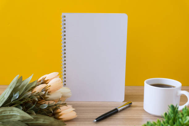 istock Notebook with coffee cup and flower on wood desk with yellow background. 1019051006
