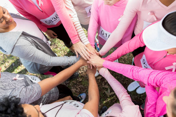 Group of unrecognizable race for the cure participants stack hands In this view from above, an unrecognizable group of race for the cure participants stand outside in a circle and stack hands. pink promise stock pictures, royalty-free photos & images