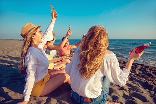 group of happy young people dancing at the beach on beautiful summer sunset