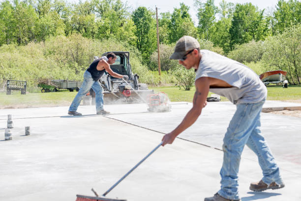 New Residential Concrete Slab with Radiant Floor Heating - Preparation and Equipment Erskine, USA - May 25, 2018: The process and equipment of preparing a private residential concrete slab foundation with a radiant floor heating system (water or propane gas). This image shows a worker operating a concrete saw. He is cutting grooves in the new foundation to prevent cracking. Another worker, in the foreground, is sweeping the dust. Focus is on the worker operating the saw. A home will be moved and placed on this slab in the near future. Driveway Installers stock pictures, royalty-free photos & images