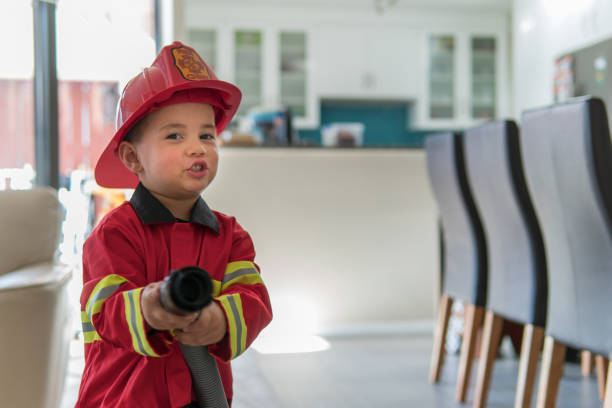 Little boy pretending to be a fireman A 3-year old eurasian boy is dressed up in a fireman costume and using a vacuum cleaner hose to pretend that he is putting out a fire fire hose photos stock pictures, royalty-free photos & images