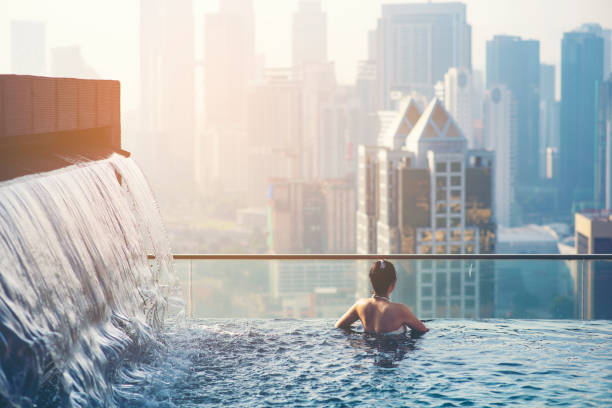 アジア旅行。屋上スイミング プールから街の風景を楽しんでいる若い女性。 - vacations infinity pool relaxation swimming pool ストックフォトと画像
