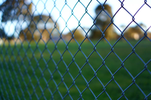 Chain link fence with empty park at background Chain link fence with blurred background of empty park wire mesh stock pictures, royalty-free photos & images