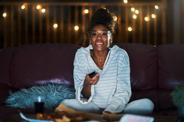 african american woman in pajamas staying up late at night eating pizza stock photo