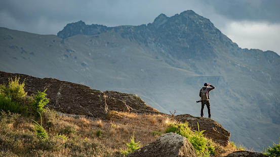 Young male photographer looking at mountain scenery during golden hour sunset on Queenstown hill in Queenstown, South Island, New Zealand. Travel and photography concept