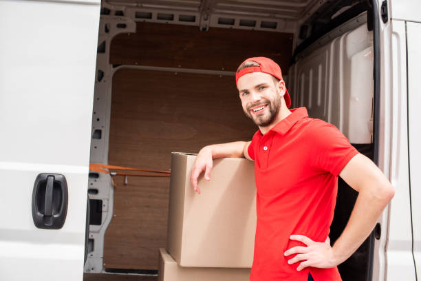 istock smiling young delivery man in uniform standing near van with cargo 1019217302