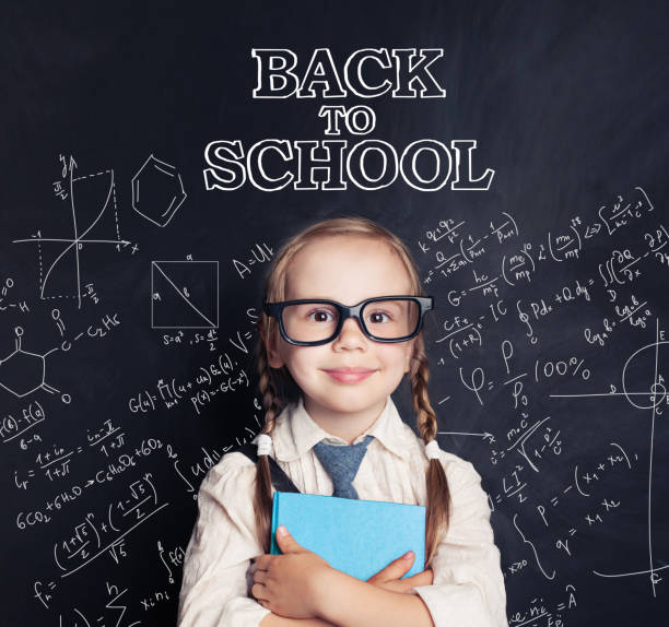 istock Happy child smiling and holding blue book on blackboard background with science chalk pattern. Back to school concept 1019219746