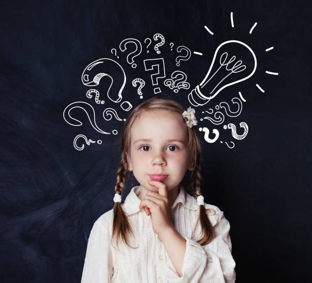 istock Smart child schoolgirl with lightbulb and chalk question marks on school blackboard background. Idea concept 1019219786