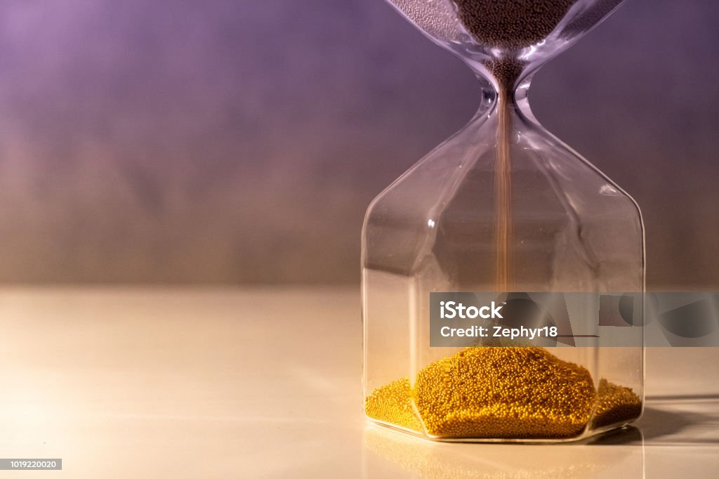 Gold sand running through the shape of modern hourglass on white table.Time passing and running out of time. Urgency countdown timer for business deadline concept Patience Stock Photo