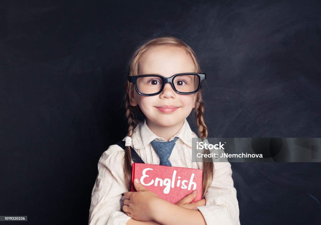 Cute child schoolgirl holding red book on chalkboard background. Speak english and learn language concept English Language Stock Photo