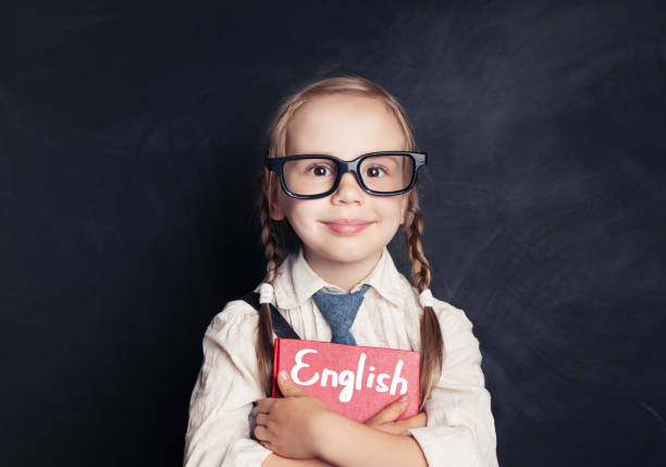可愛的兒童女學生持有紅色的書黑板背景。講英語和學習語言概念 - 英語 個照片及圖片檔