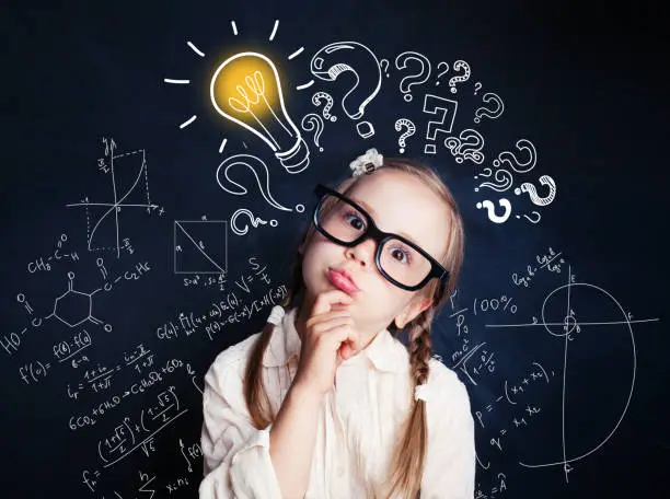 Photo of Small child mathematics student thinking on background with lightbulb and math formulas. Kid ideas