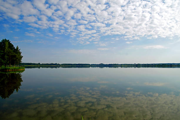 A summer quiet day on a forest lake. Clouds are reflected on the water surface  blue sky and clouds