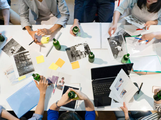 Magazine Editors At Work. Magazine editors brainstorming with drinking bottle of alcohol. Discussing and looking for new ideas for their magazine. office fun business adhesive note stock pictures, royalty-free photos & images