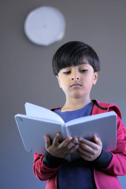 Young child reading book with wall clock in background Portrait of young kid reading book with wall clock in background. Child studying with wall clock behind. clock wall clock face clock hand stock pictures, royalty-free photos & images