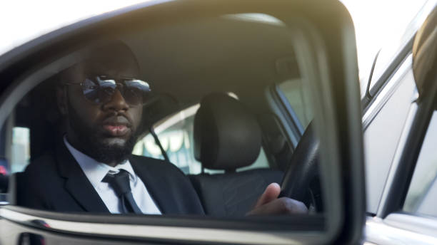 istock Black man in sunglasses driving car, looking in side-view mirror, bodyguard 1019313094