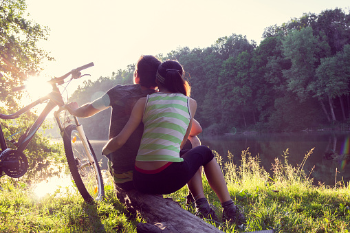 couple is embrace each other sits on the river bank with bicycle