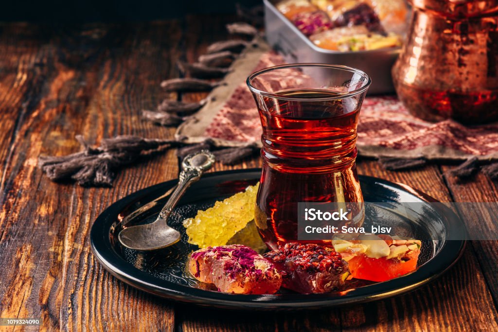 Tea in armudu with oriental delight Tea in armudu glass with oriental delight rahat lokum on metal tray over wooden surface and tablecloth Tea - Hot Drink Stock Photo