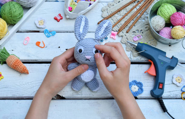 istock Making rabbit with carrot. Crochet bunny for child. On table threads, needles, hook, cotton yarn. Step 3 - glue eyes of toy. Handmade crafts. DIY concept. Small business. Income from hobby. 1019329322