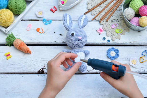 istock Making rabbit with carrot. Crochet bunny for child. On table threads, needles, hook, cotton yarn. Step 3 - glue eyes of toy. Handmade crafts. DIY concept. Small business. Income from hobby. 1019330774