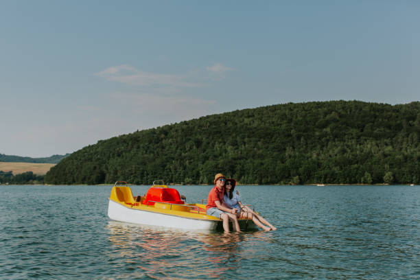 Couple in love resting on pedal boat with feet in water. Smiling man and woman hugging while boating on the lake. paddleboat stock pictures, royalty-free photos & images