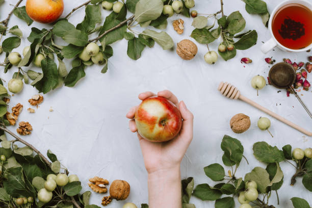 istock Warm autumn flatlay with apple branches, fruits, walnuts, red tea in a cup and woman's hand on grey cement background 1019335796