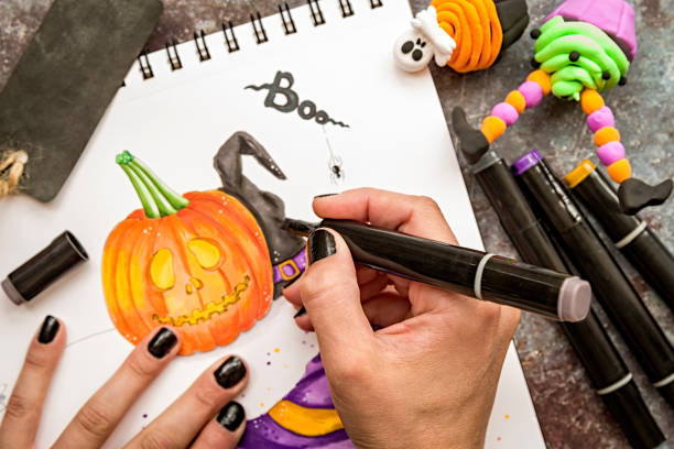 female hands with black nails drawing halloween illustration with markers on wooden table top view halloween concept. female hands with black nails drawing halloween illustration with markers on wooden table top view polymer clay sweets stock pictures, royalty-free photos & images