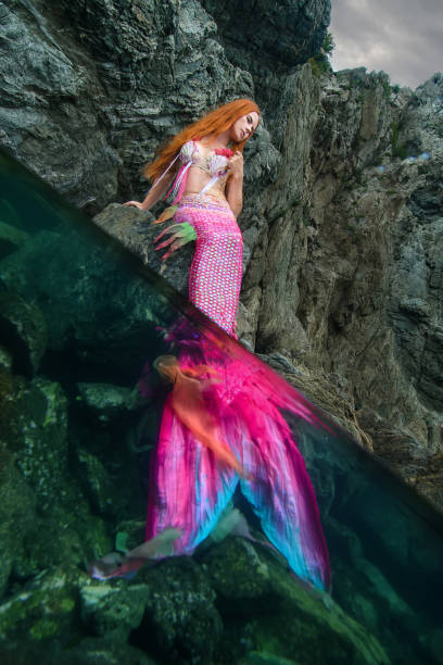 istock Beautiful mermaid with long tail on sea shore 1019375890