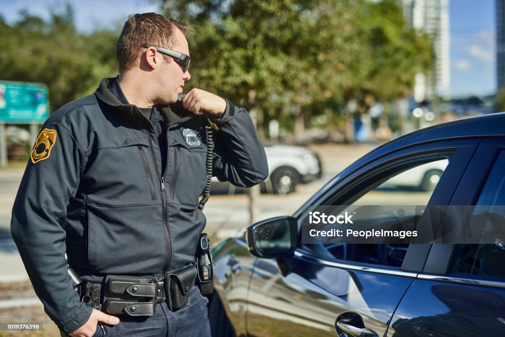 Come in dispatch Cropped shot of a handsome young policeman radioing in with headquarters Police Force Stock Photo