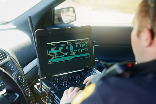 Cropped shot of an unrecognizable male police officer using his laptop while out on patrol