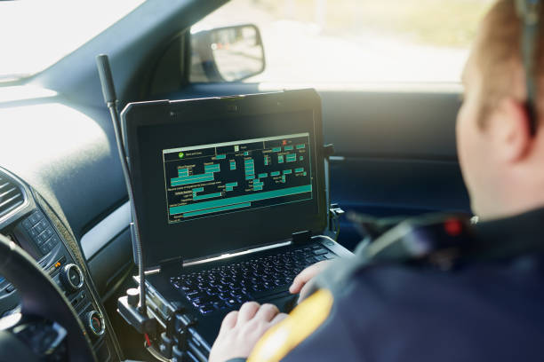 Logging in to the police database Cropped shot of an unrecognizable male police officer using his laptop while out on patrol police car technology stock pictures, royalty-free photos & images