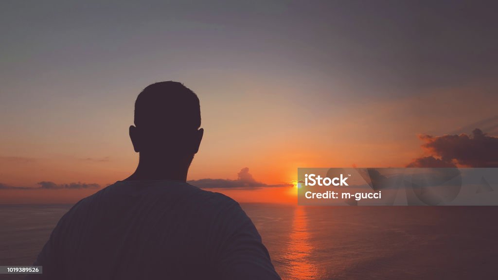 Silhouette of man in sunset / sunrise time over the ocean. Loneliness Stock Photo