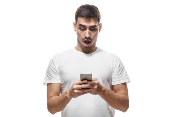 istock Handsome young man in white t-shirt, holding smartphone, looking scared and confused reading text message or e-mail 1019406598