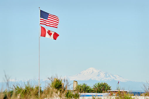 US and Canadian Flags fly in Point Roberts, Washington State. The San Juan Islands in the background.