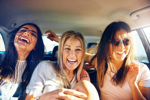 Three vivacious girlfriends on a road trip together sitting as passengers in the back of the car giggling and laughing with pleasure and enjoyment