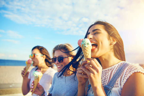 Three young woman eating ice cream at the seaside Three young woman eating ice cream cones at the seaside as they stroll along a waterfront promenade on a hot summer day during their vacation licking ice cream cone stock pictures, royalty-free photos & images