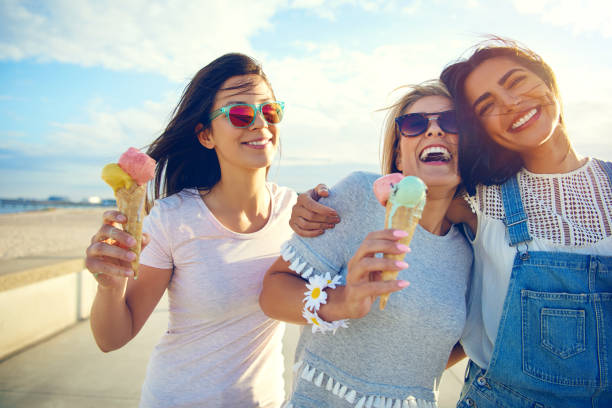 Laughing teenage girls enjoying ice cream cones Laughing teenage girls eating ice cream cones as they walk along a beachfront promenade arm in arm enjoying their summer vacation beach fun stock pictures, royalty-free photos & images