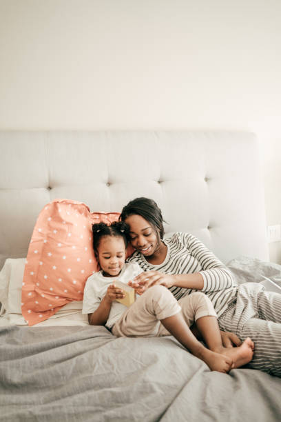 Reading and learning at home Mom and her toddler daughter reading a small book in bed. bedtime photos stock pictures, royalty-free photos & images