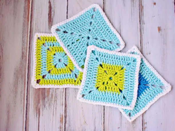 Bright blue and green squares crocheted in cotton yarn, laying on a white wood tabletop.