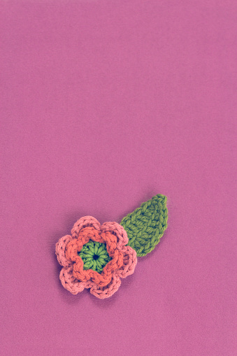 Pink flower, handmade crocheted accessory, laying on a purple paper background.