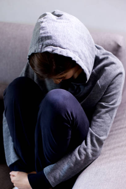 istock Sad young woman with hood sitting on sofa depressed medium shot 1019441508