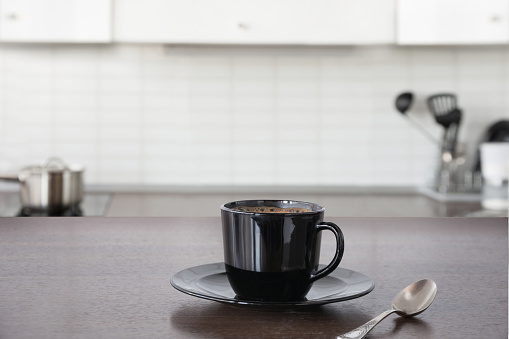 Cup of hot coffee on wooden board. Blurred kitchen as background.