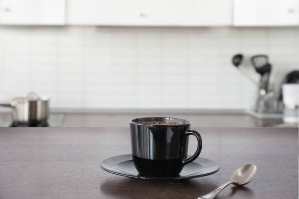 Cup of coffee on wooden board. Blurred kitchen as background. Cup of hot coffee on wooden board. Blurred kitchen as background. black coffee stock pictures, royalty-free photos & images