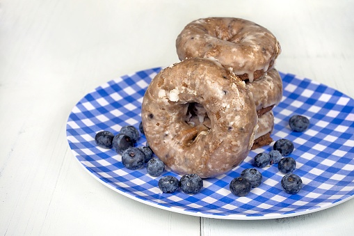 blueberry donuts with ripe berries on blue and white checkered plate on wood