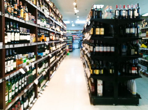 Blurred image of wine shelves display in supermarket. Defocused Rows of Wine Liquor bottles on the store shelf. Alcoholic beverage abstract background. Alcohol drink market concept.Blur Background  alcohol Shelves .