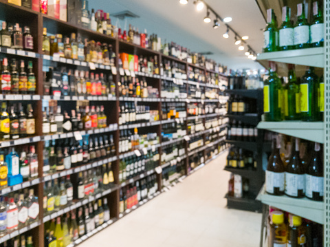 Blurred image of wine shelves display in supermarket. Defocused Rows of Wine Liquor bottles on the store shelf. Alcoholic beverage abstract background. Alcohol drink market concept.Blur Background  alcohol Shelves .